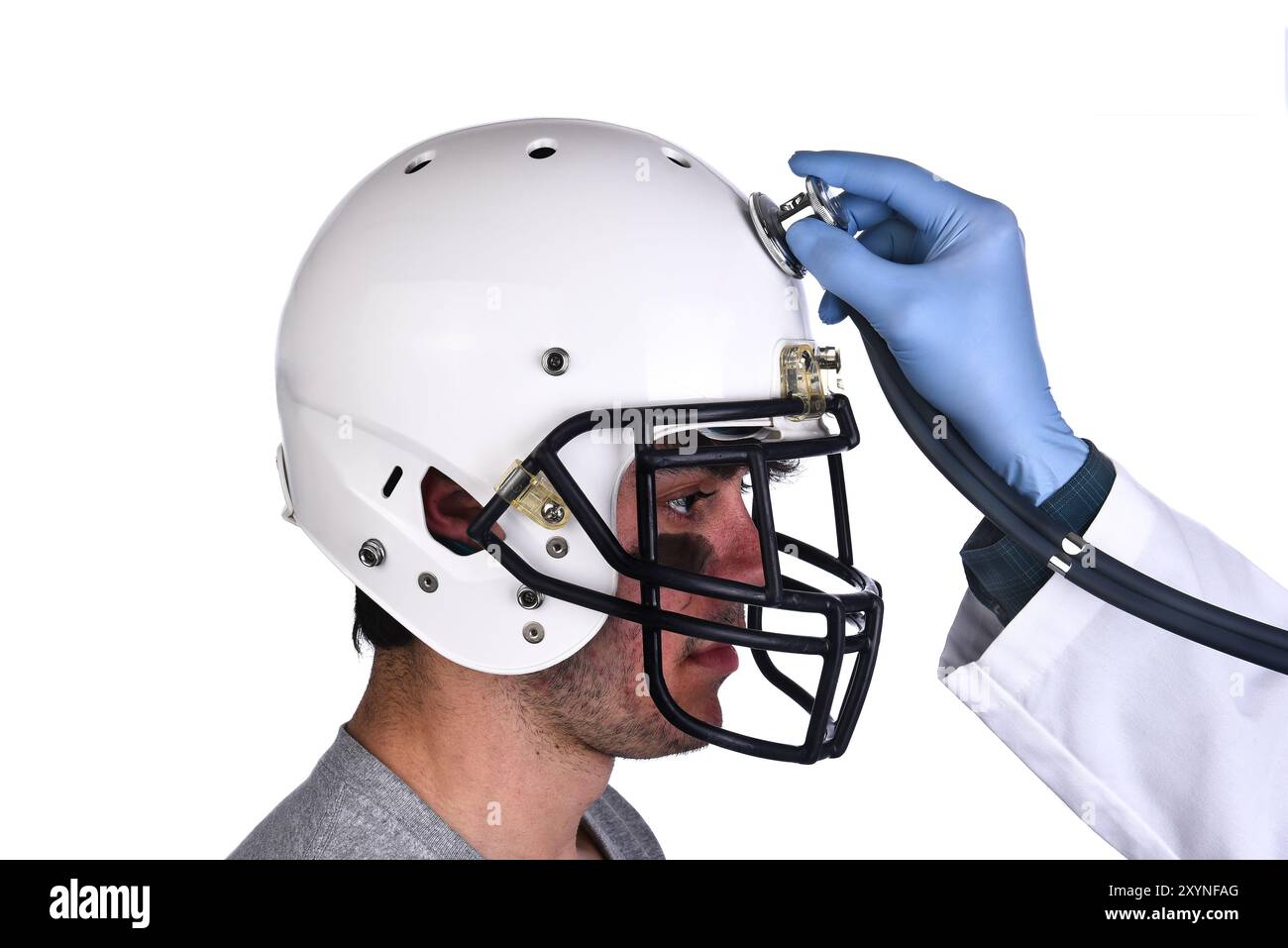 Un giocatore di calcio che indossa un casco con la mano del medico che regge uno stetoscopio sulla corona del casco. Concetto di commozione cerebrale sportiva e relative condizioni Foto Stock