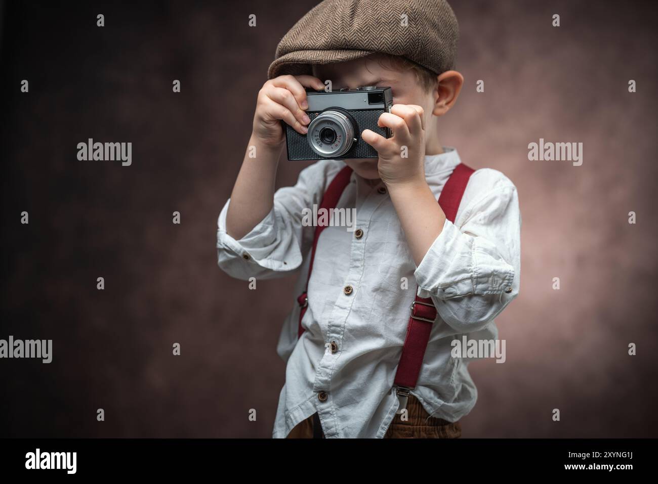 Fotografo ragazzo con fotocamera retrò che crea immagini su sfondo vintage Foto Stock