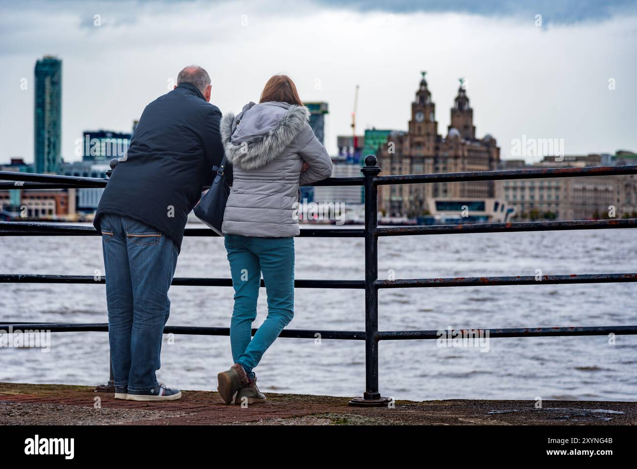 Una giornata fredda per questa coppia che guarda il fegato reale che si estende sul fiume Mersey. Foto Stock
