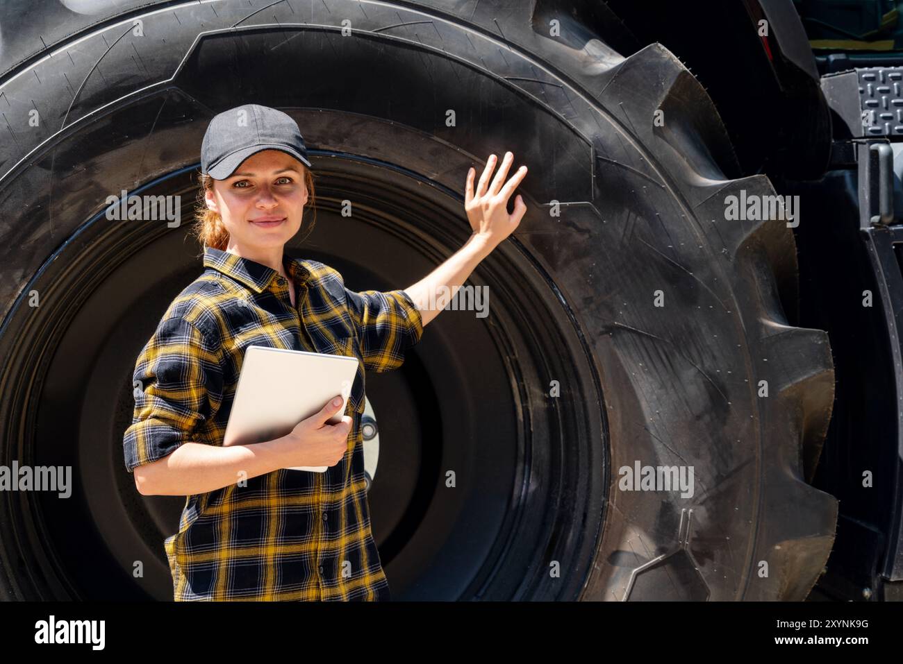 Una donna con un tablet digitale in mano tocca una grande ruota di una macchina da costruzione o agricola. Foto Stock