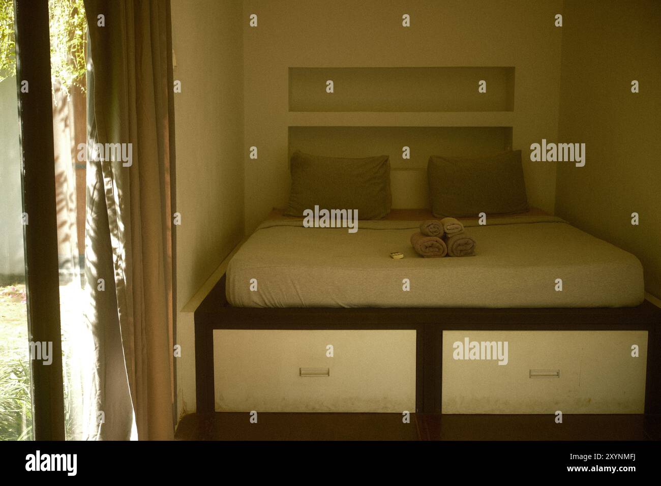 Interno della camera da letto con vano sotto il letto, nicchia a parete e riflesso della luce solare dalla porta di vetro Foto Stock