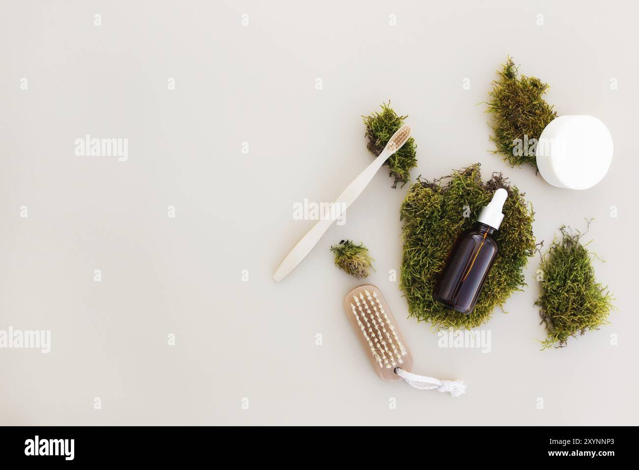 Concetto sanitario di accessori da bagno flay con bottiglia di olio essenziale, spazzolino da denti in legno, spazzola per i piedi, sapone su sfondo beige e muschio verde A. Foto Stock