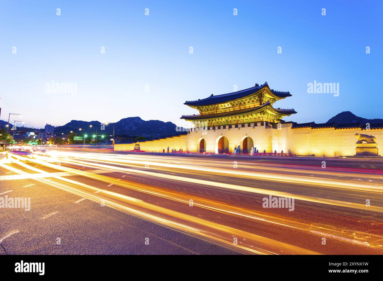 Fari colorati di auto che passano davanti al cancello illuminato di Gwanghuamun, ingresso allo storico Palazzo Gyeongbokgung al crepuscolo in basso Foto Stock