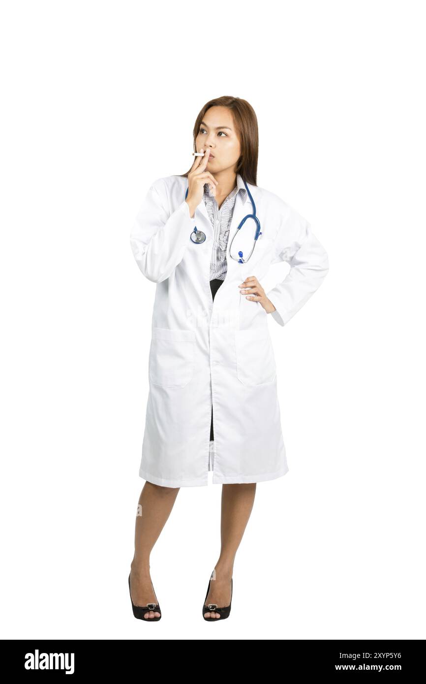Una bella donna asiatica si trova casualmente, ironicamente fumando sigaretta guardando lontano braccio akimbo mostrando un'abitudine malsana. Verbale a tutta lunghezza Foto Stock