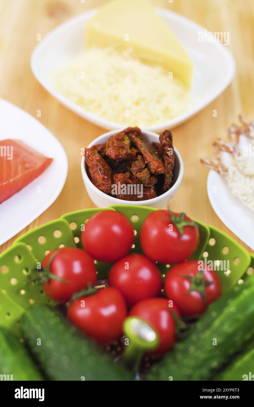 Natura morta del cibo crudo in piatti bianchi su un tavolo di legno. Salmone congelato su un piatto accanto a cetrioli e pomodori formaggio grattugiato e gamberetti crudi in bre Foto Stock