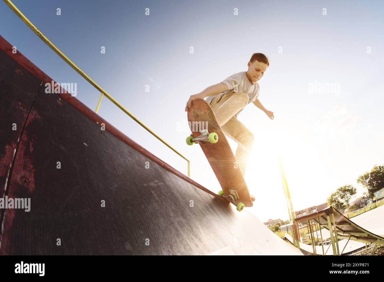 Il pattinatore teenager è appeso su una rampa su uno skateboard in uno skate Park al tramonto. Grandangolo Foto Stock