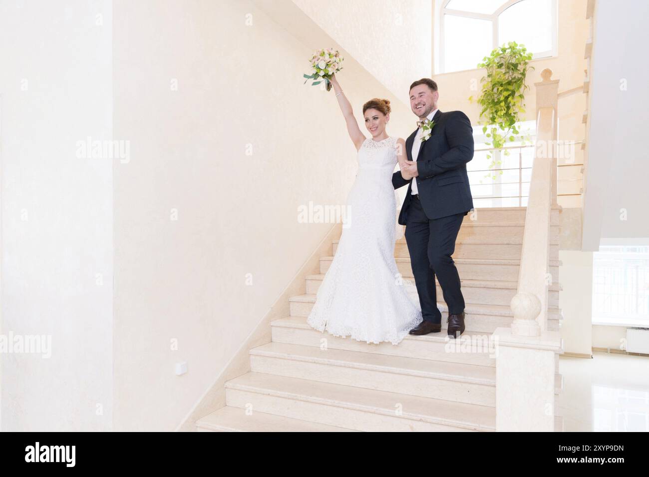 Un paio di sposi novelli scendono le scale nell'ufficio del registro e salutano coloro che li incontrano con sorrisi e gesti. Il concetto di matrimonio in Th Foto Stock