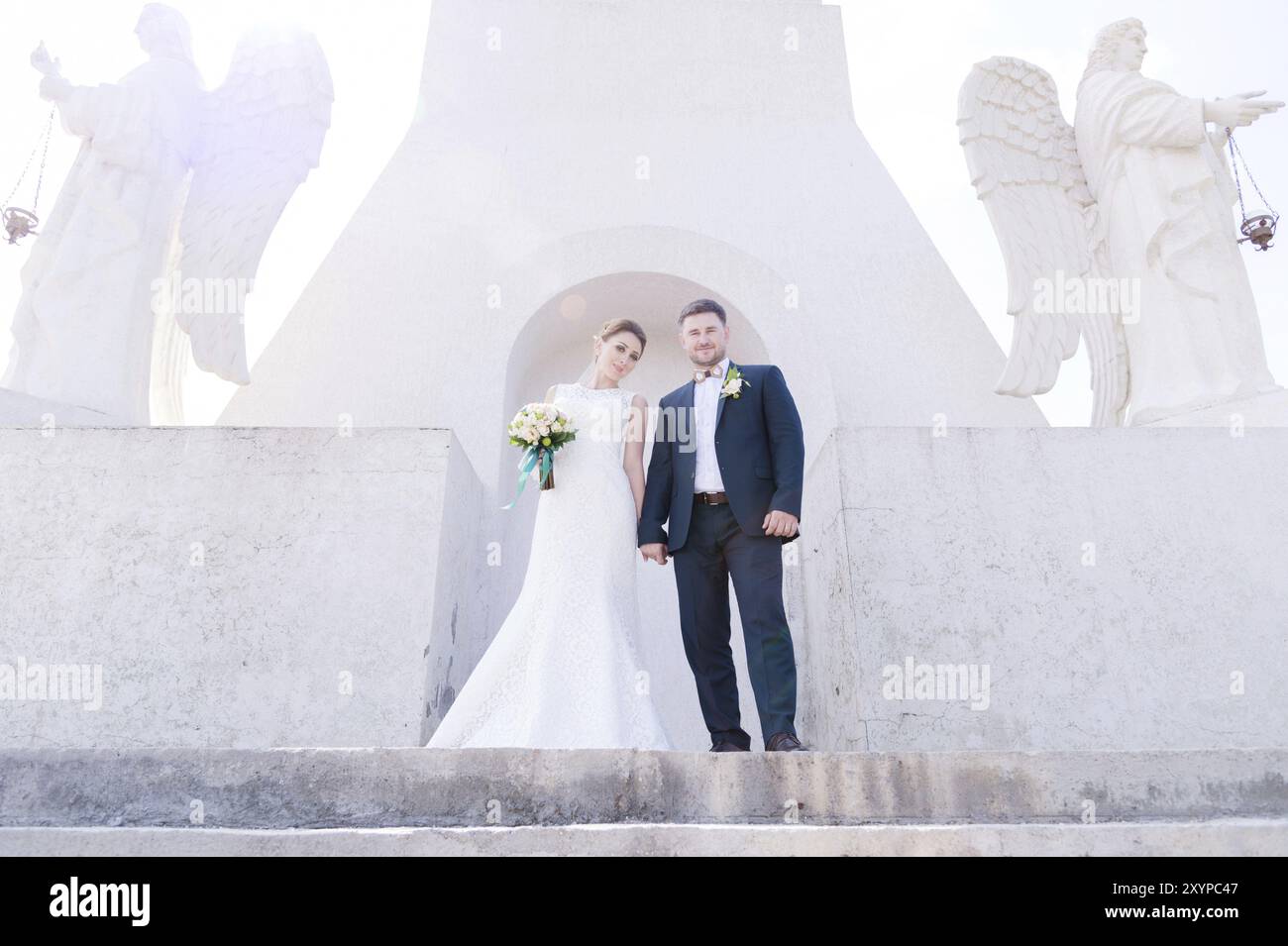 Ritratto di una bella coppia in luna di miele in un giorno di nozze con un bouquet in mano sullo sfondo di un monumento cristiano ortodosso con angeli. Foto Stock