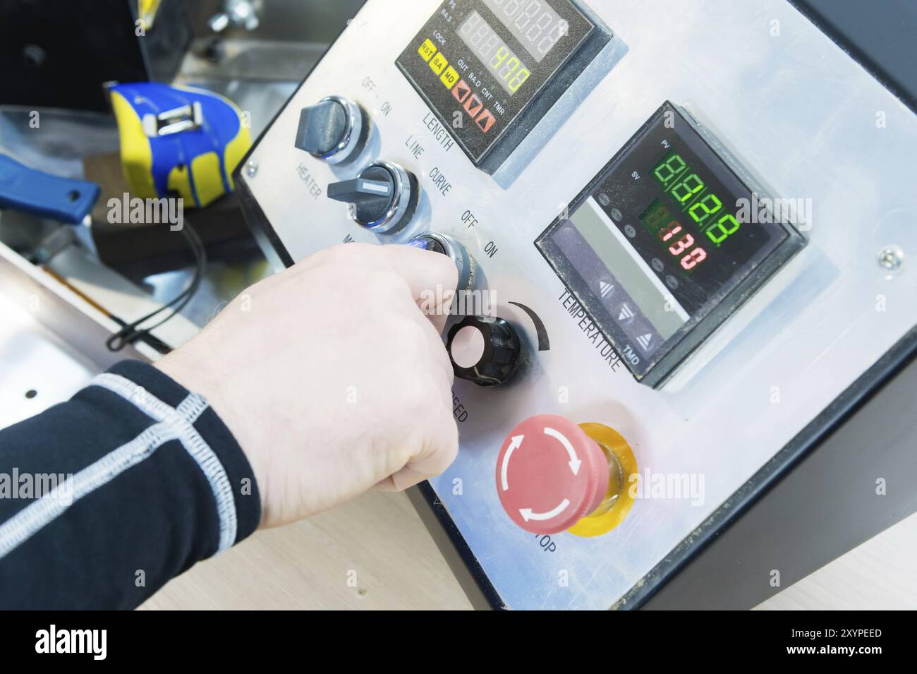 Un primo piano della mano di un uomo tiene un interruttore rotativo sul pannello di controllo dell'attrezzatura con gli strumenti Foto Stock