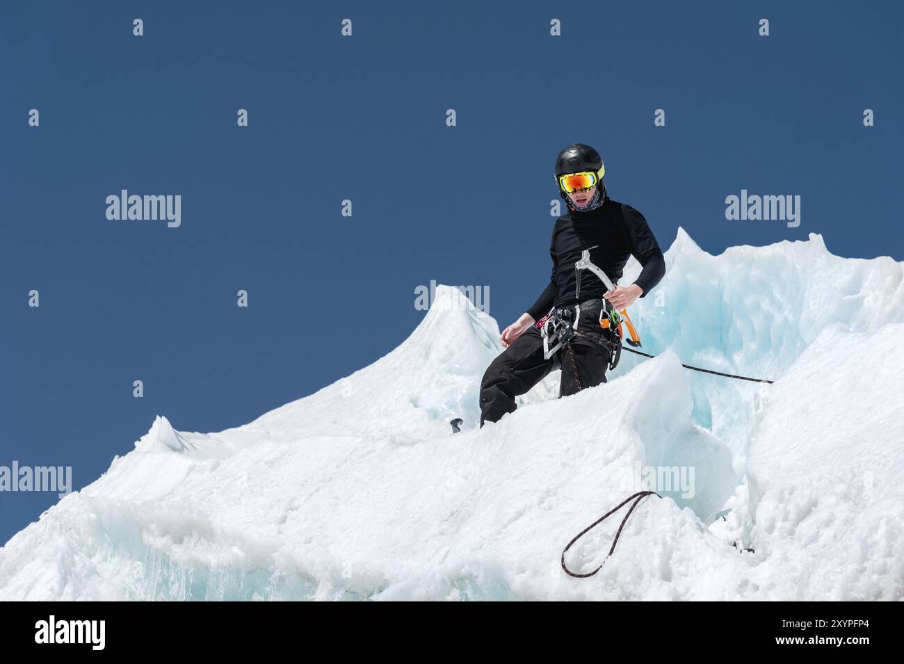 Un alpinista professionista con casco e maschera da sci sull'assicurazione fa intagliare l'ascia di ghiaccio nel ghiacciaio. Il lavoro di un alpinista professionista in winte Foto Stock