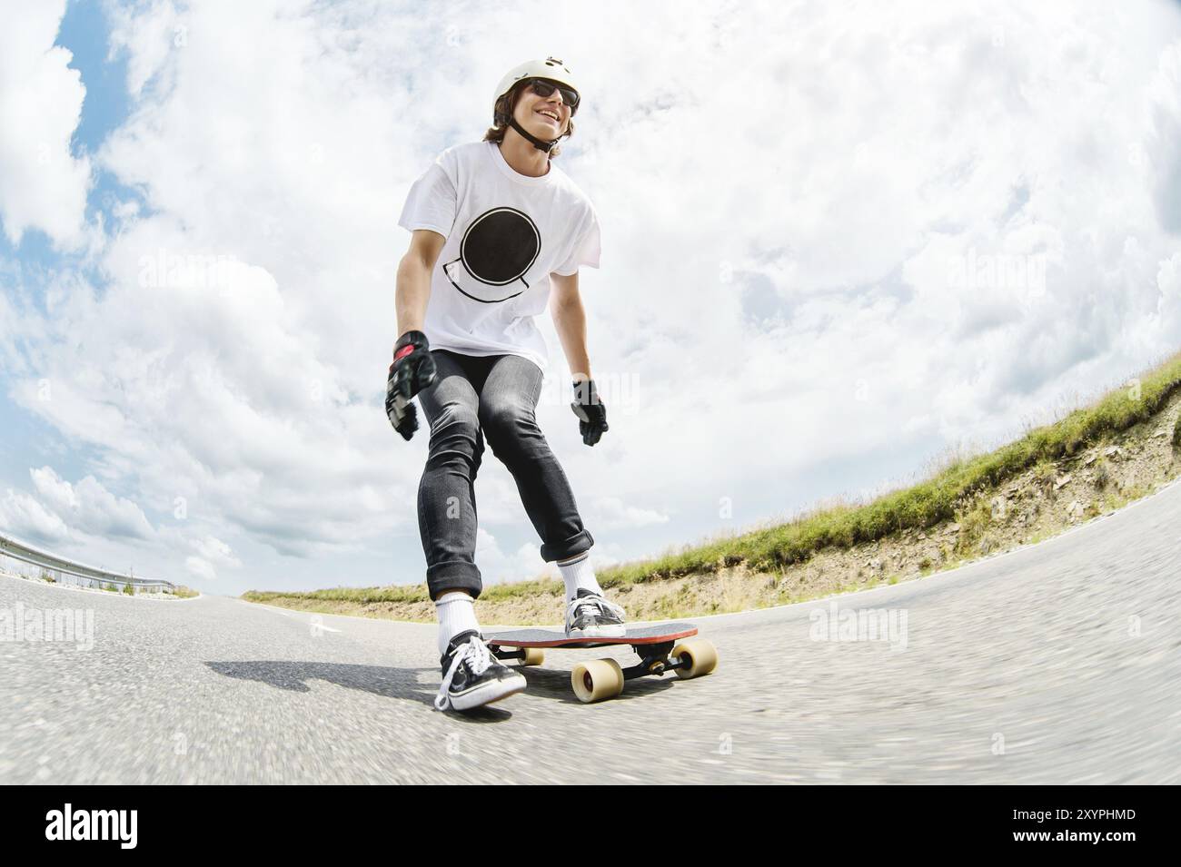 Un giovane Longboarder spinge il piede sul suo lungolago lungo la strada di campagna sullo sfondo del paesaggio caucasico Foto Stock