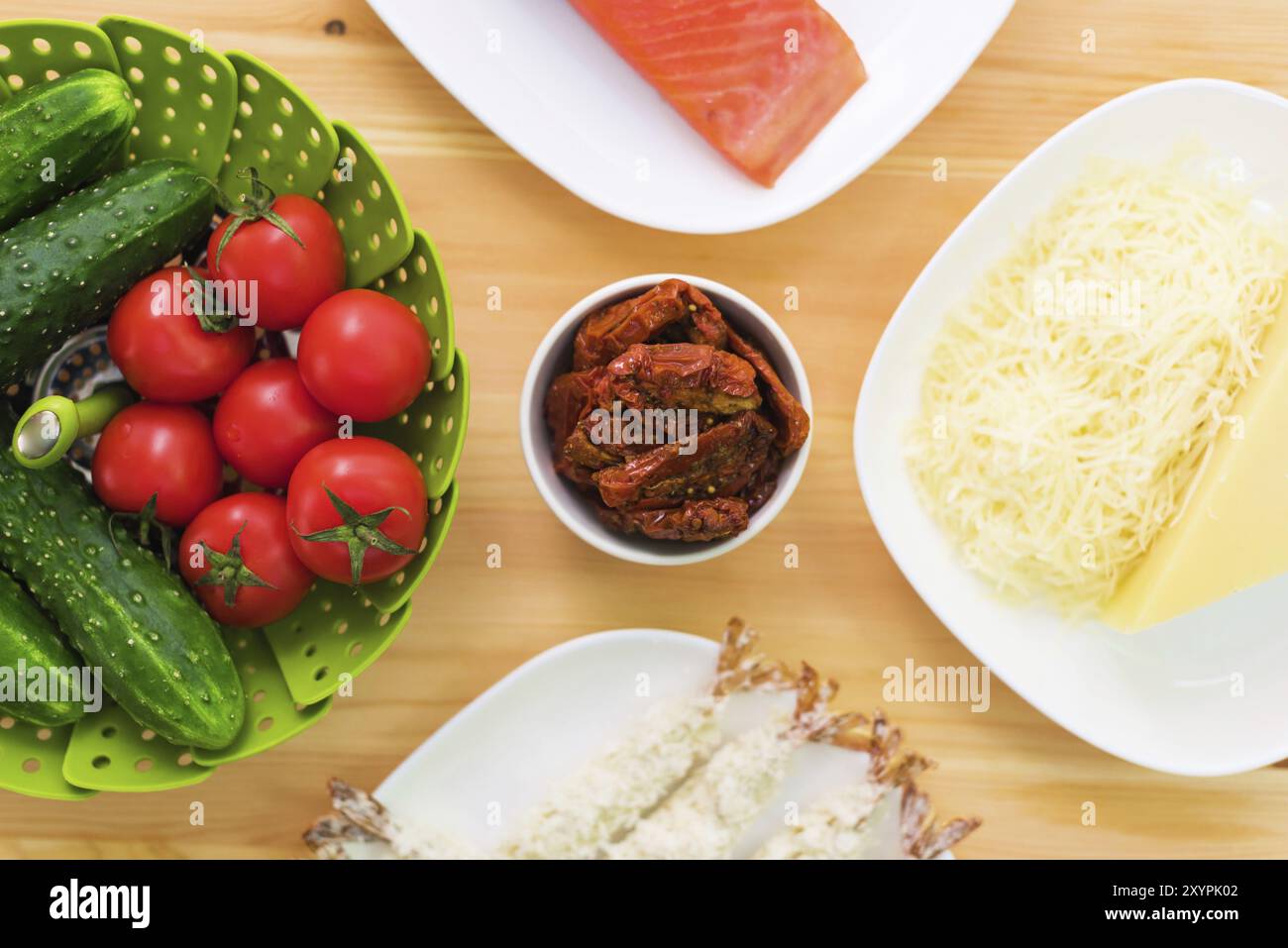 Natura morta del cibo crudo in piatti bianchi su un tavolo di legno. Salmone congelato su un piatto accanto a cetrioli e pomodori formaggio grattugiato e gamberetti crudi in bre Foto Stock