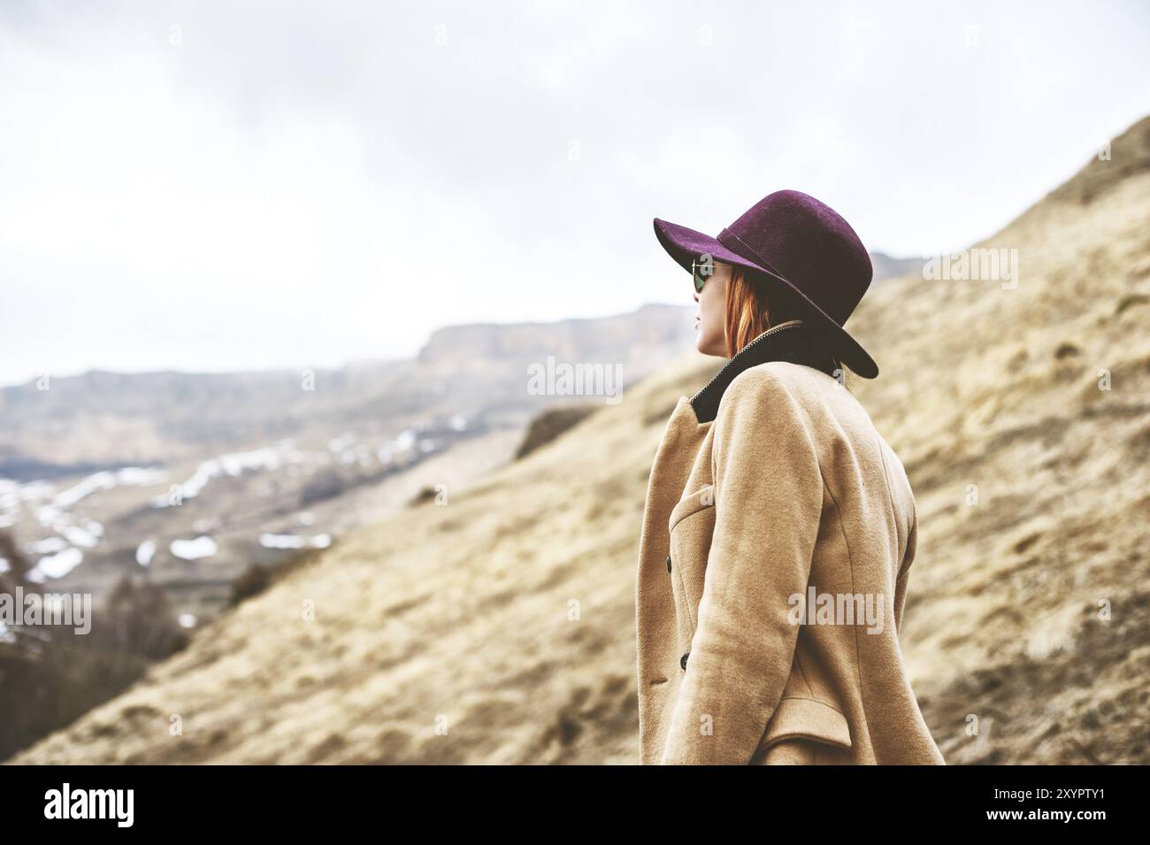 Una ragazza in stile classico, un cappello e un cappotto sulle montagne caucasiche in una serata nebbiosa Foto Stock