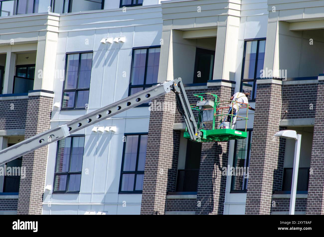 Operaio edile sul sollevamento del braccio che esegue la manutenzione degli esterni – sicurezza e riparazione degli edifici urbani Foto Stock