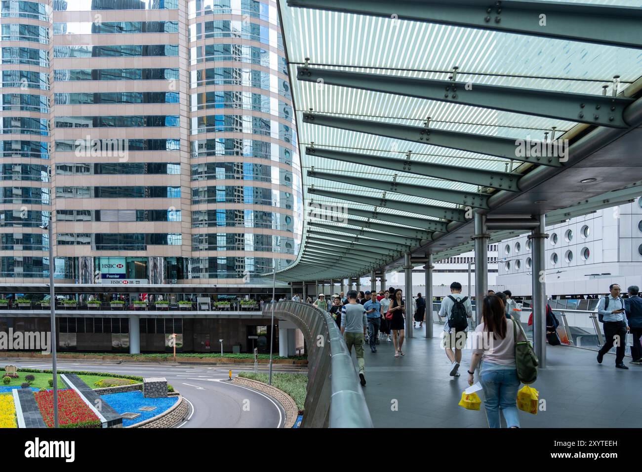 Hong Kong, Cina - 3 luglio 2024: Un ponte pedonale collega due grattacieli nella parte centrale di Hong Kong, Cina. Le persone attraversano il ponte con l'informatore Foto Stock