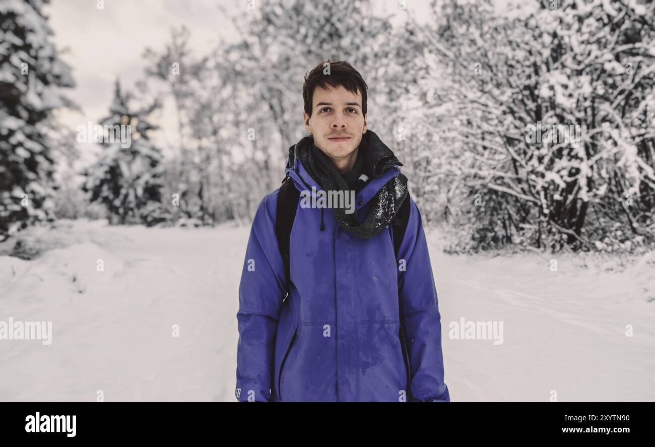 Giovane uomo adulto con capelli corti marroni in piedi in uno splendido paesaggio di neve durante l'inverno in norvegia, indossando una giacca da pioggia blu, guardando la macchina fotografica, NOR Foto Stock