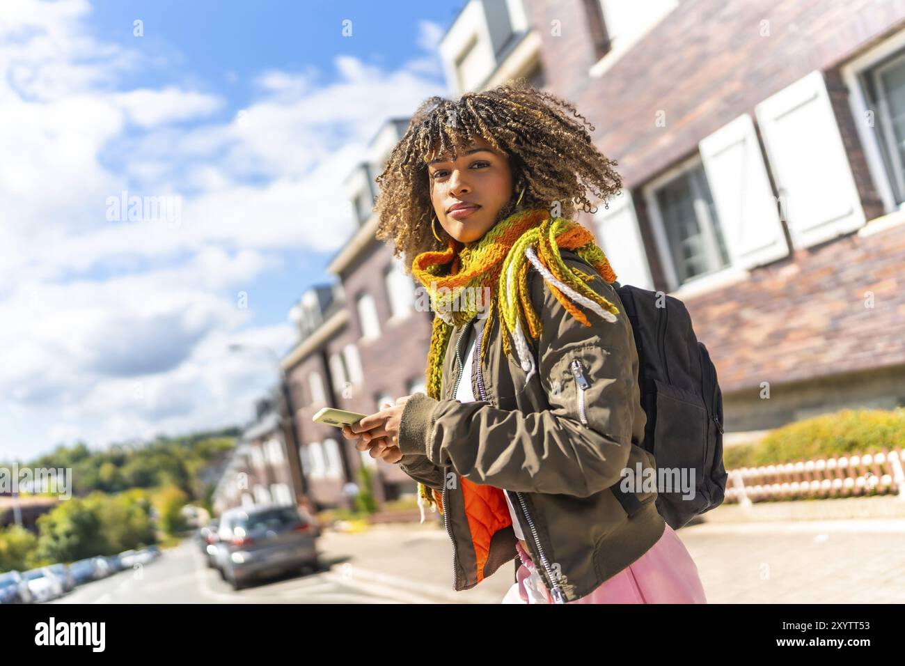 Giovane donna vitale che guarda la fotocamera mentre usa il telefono in città Foto Stock