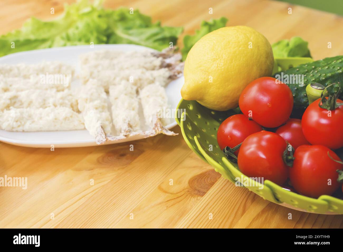 Gamberi crudi in pastella pronti per la tostatura accanto a un cestino di cetrioli e cetrioli di limone e pomodori sullo sfondo di foglie di lattuga su un legno Foto Stock