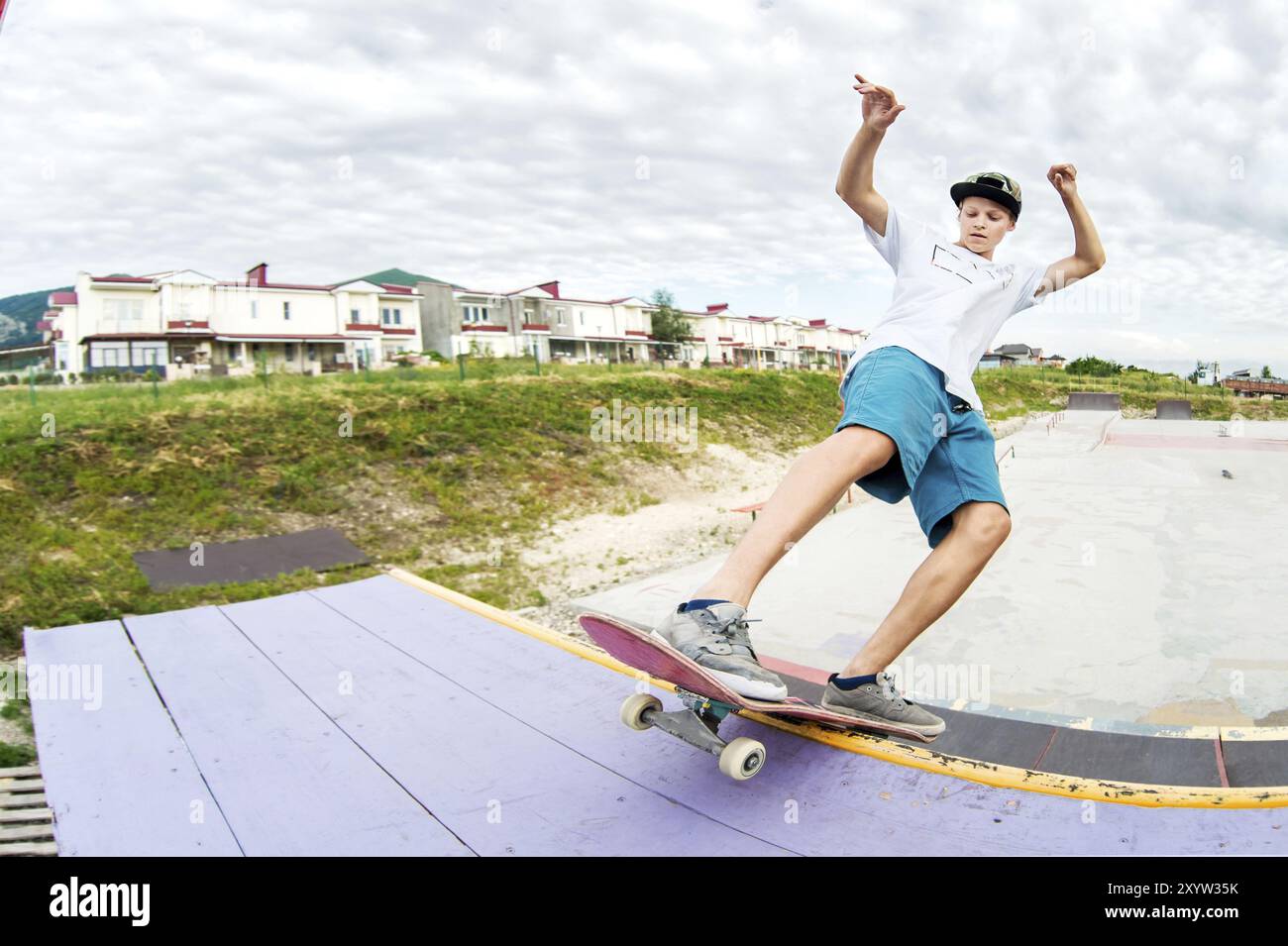 Skater adolescente in berretto e pantaloncini su rotaia su uno skateboard in un parco di skate grandangolare Foto Stock