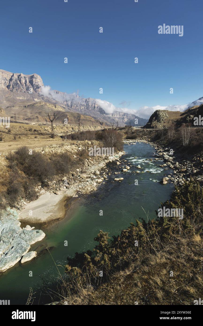 Un fiume di montagna in un'area rocciosa montuosa vicino alla quale ci sono linee elettriche sullo sfondo di rocce epiche e un cielo blu. Concetto di fornitura di energia Foto Stock