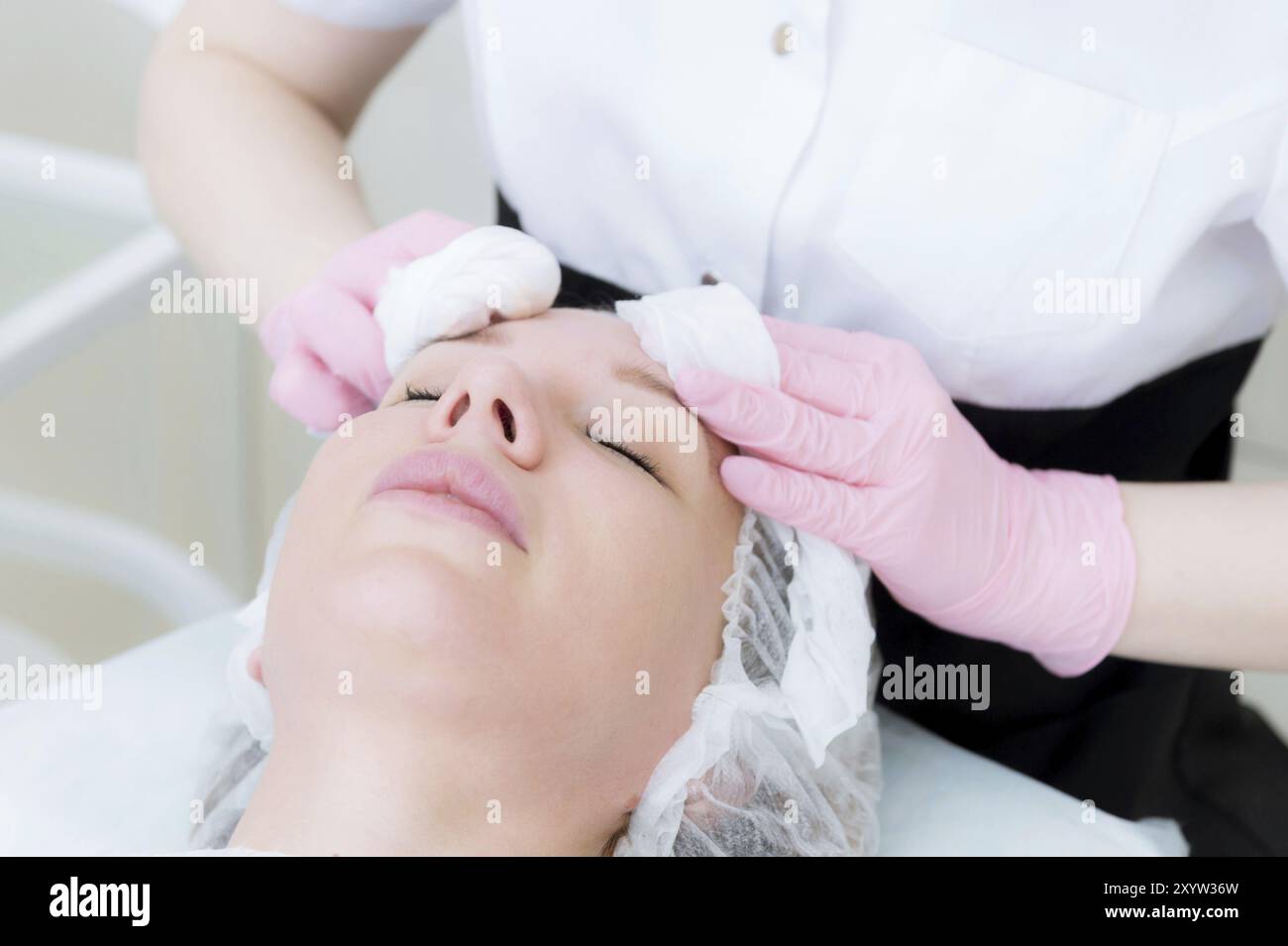 Un primo piano della procedura di pulizia nell'ufficio di cosmetologia. Le mani del cosmetologo in guanti rosa sono rimosse dal viso di un giovane Foto Stock