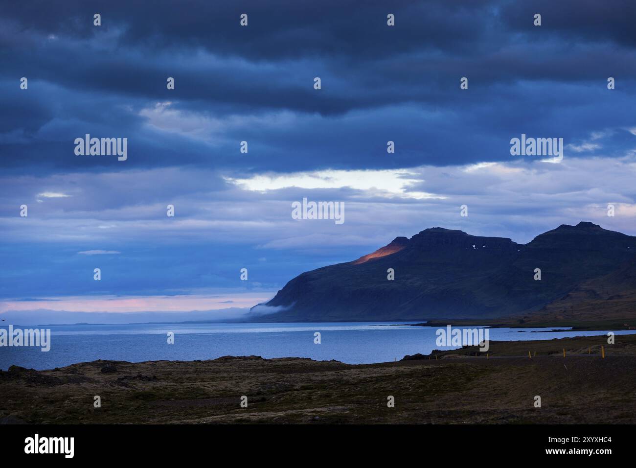 Fiordo con un cielo blu coperto e una macchia solare rossa su una montagna in Islanda Foto Stock