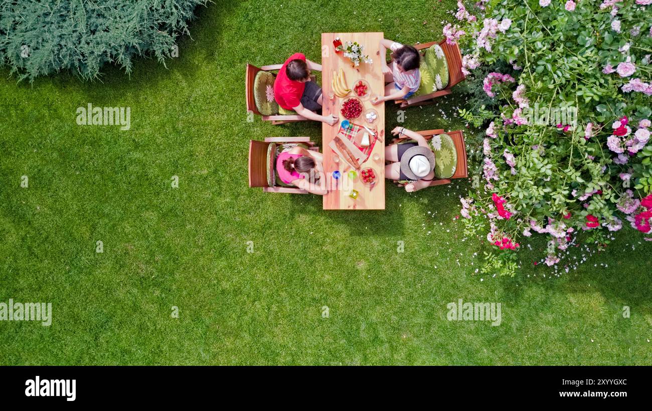 La famiglia e gli amici mangiano insieme all'aperto durante la festa estiva in giardino. Vista aerea del tavolo con cibo e bevande dall'alto. Tempo libero, vacanze e picnic Foto Stock