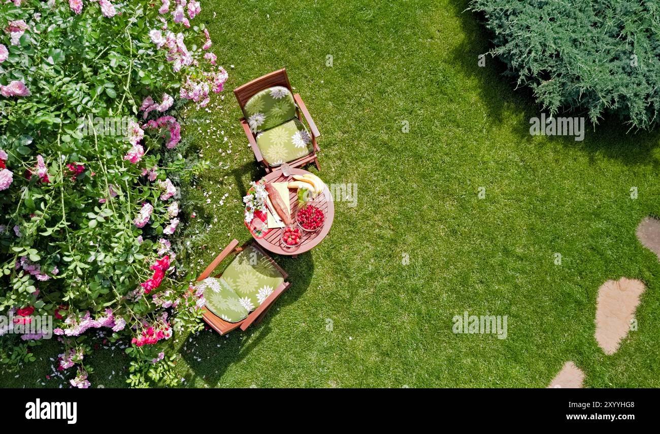 Tavolo decorato con pane, fragole e frutta nello splendido giardino di rose estivo, vista dall'alto del romantico tavolo da pranzo per due Foto Stock