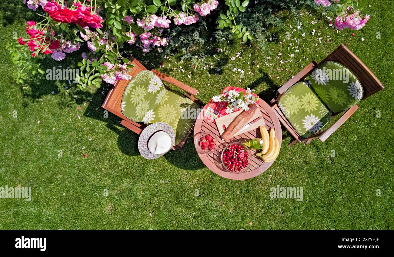 Tavolo decorato con pane, fragole e frutta nello splendido giardino di rose estivo, vista dall'alto del romantico tavolo da pranzo per due Foto Stock