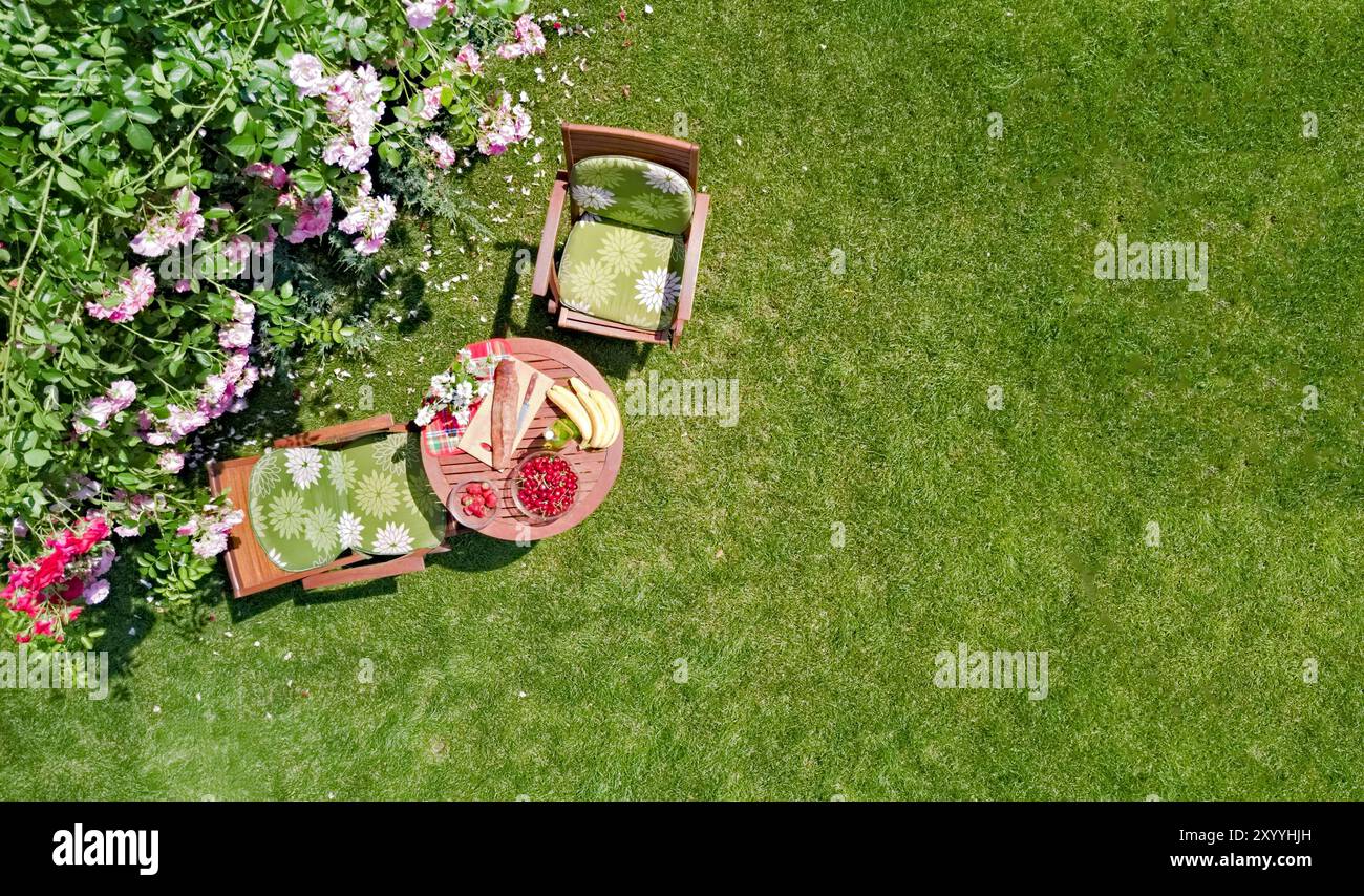 Tavolo decorato con pane, fragole e frutta nello splendido giardino di rose estivo, vista dall'alto del romantico tavolo da pranzo per due Foto Stock