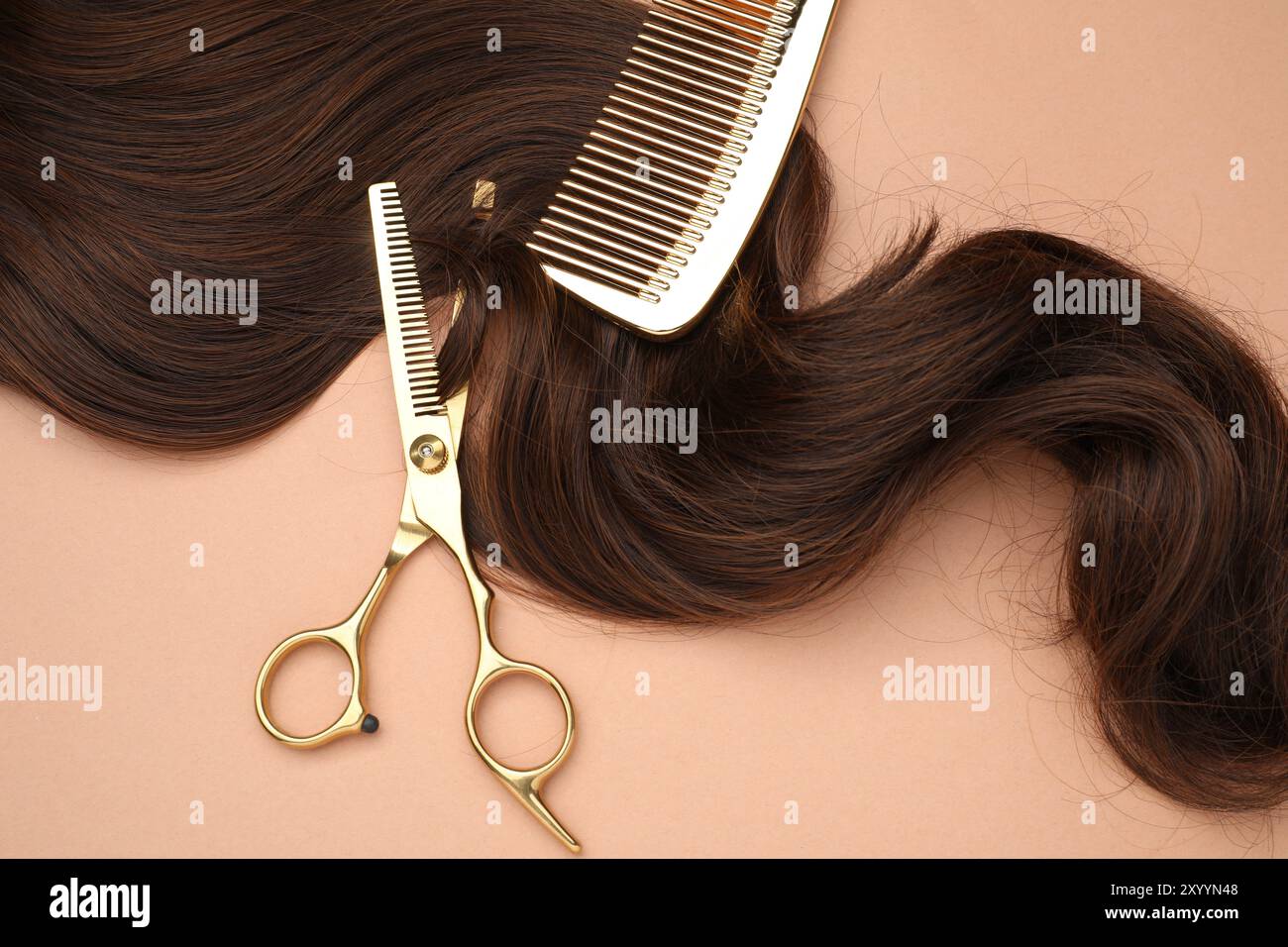 Ciocca di capelli marrone, pettine e forbici professionali su sfondo corallino chiaro, vista dall'alto Foto Stock