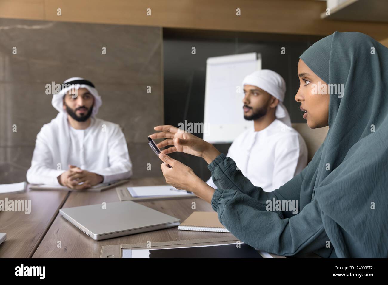 Bella donna d'affari araba seria che indossa hijab, parla con colleghi maschi Foto Stock