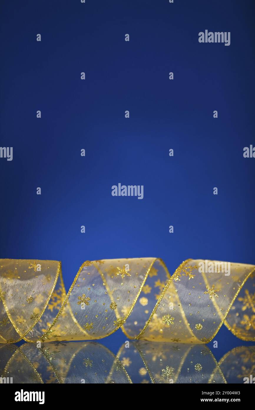 Bordo natalizio con nastro in oro su sfondo blu scuro con riflessi. DOF poco profondo Foto Stock