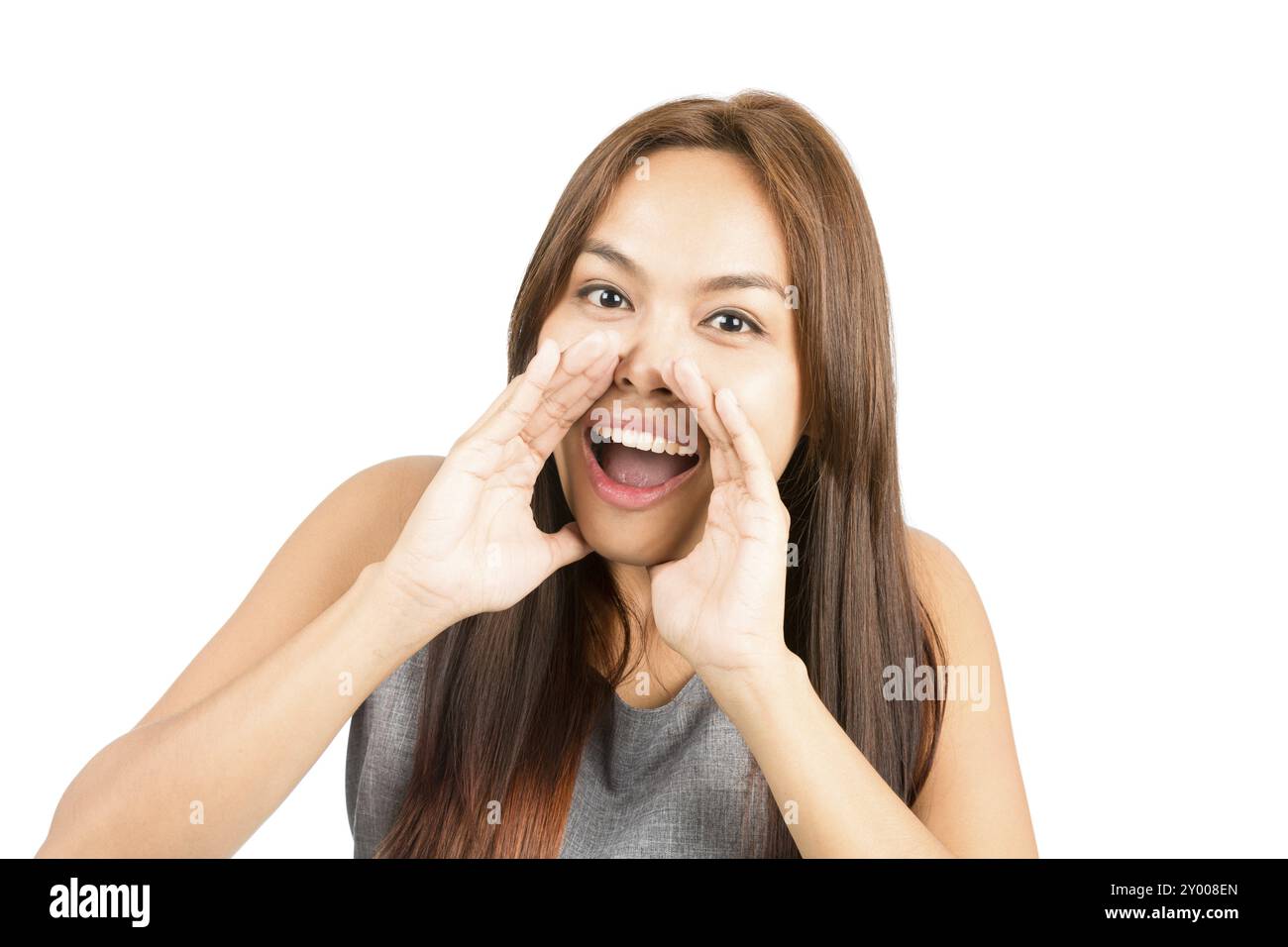 Ritratto di una bella ragazza asiatica, top senza maniche, capelli marrone chiaro che urlano annuncio guardando la fotocamera, mani accarezzate intorno alla bocca amplificando così Foto Stock