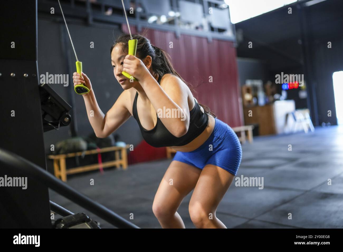 Donna cinese che usa la macchina lat per tirare pesi in una moderna palestra per il cross training Foto Stock