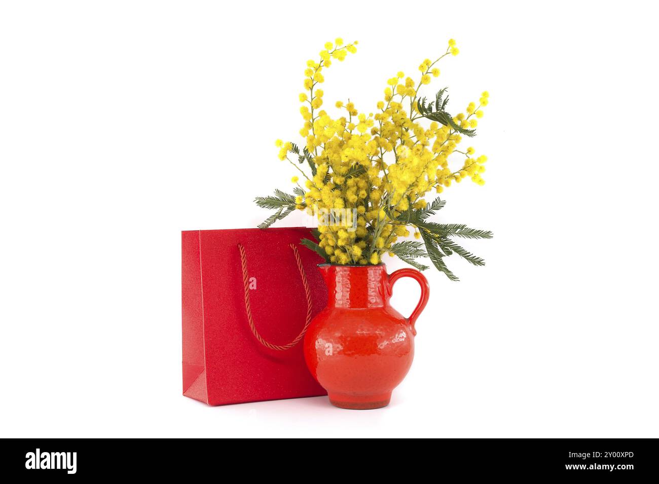 Bouquet di fiori Mimosa in vaso rosso vicino a borsa regalo rossa isolata su sfondo bianco, Pasqua, 8 marzo concetto di festa delle donne Foto Stock
