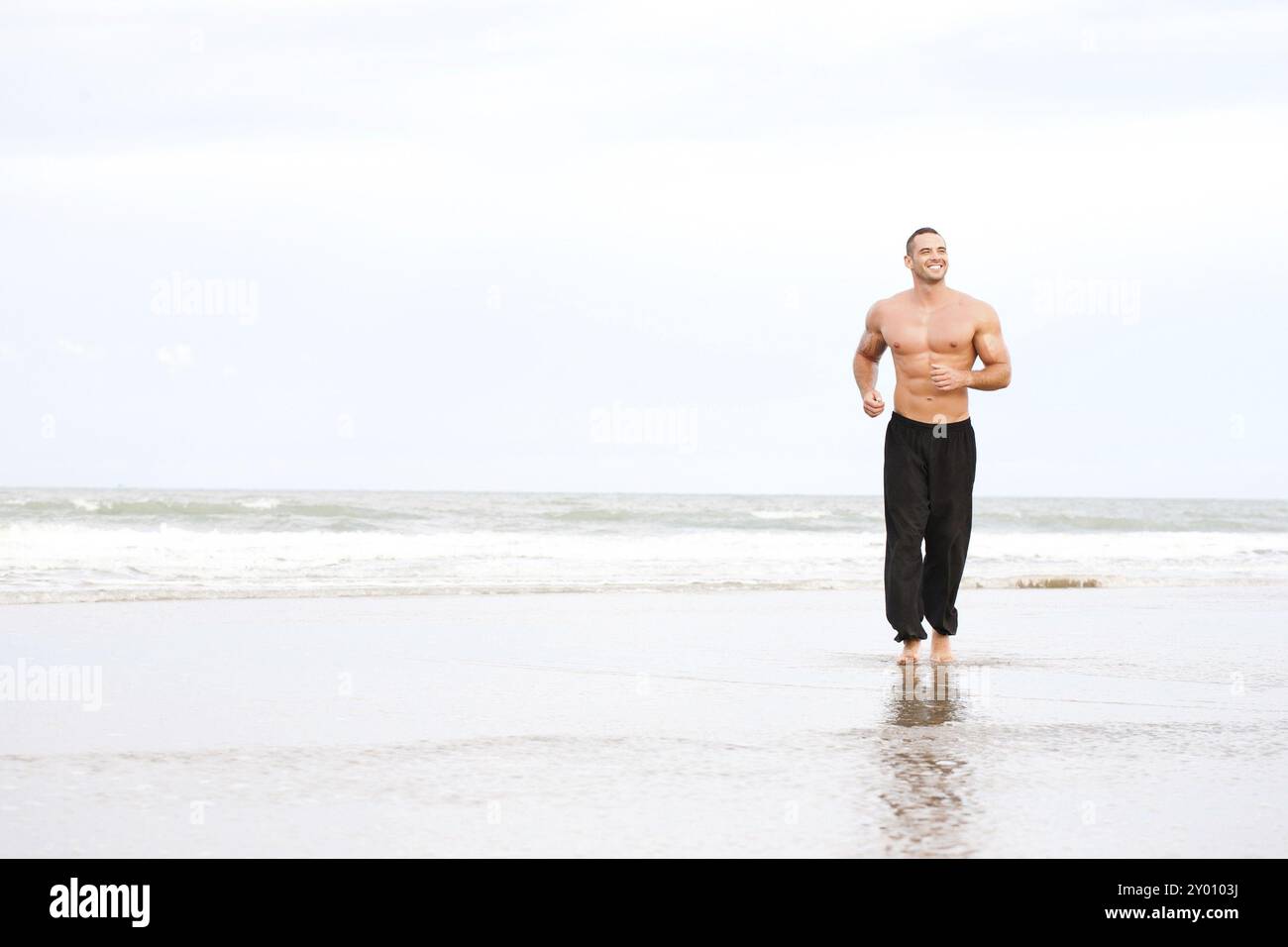 Giovane uomo muscoloso che corre sulla spiaggia Foto Stock