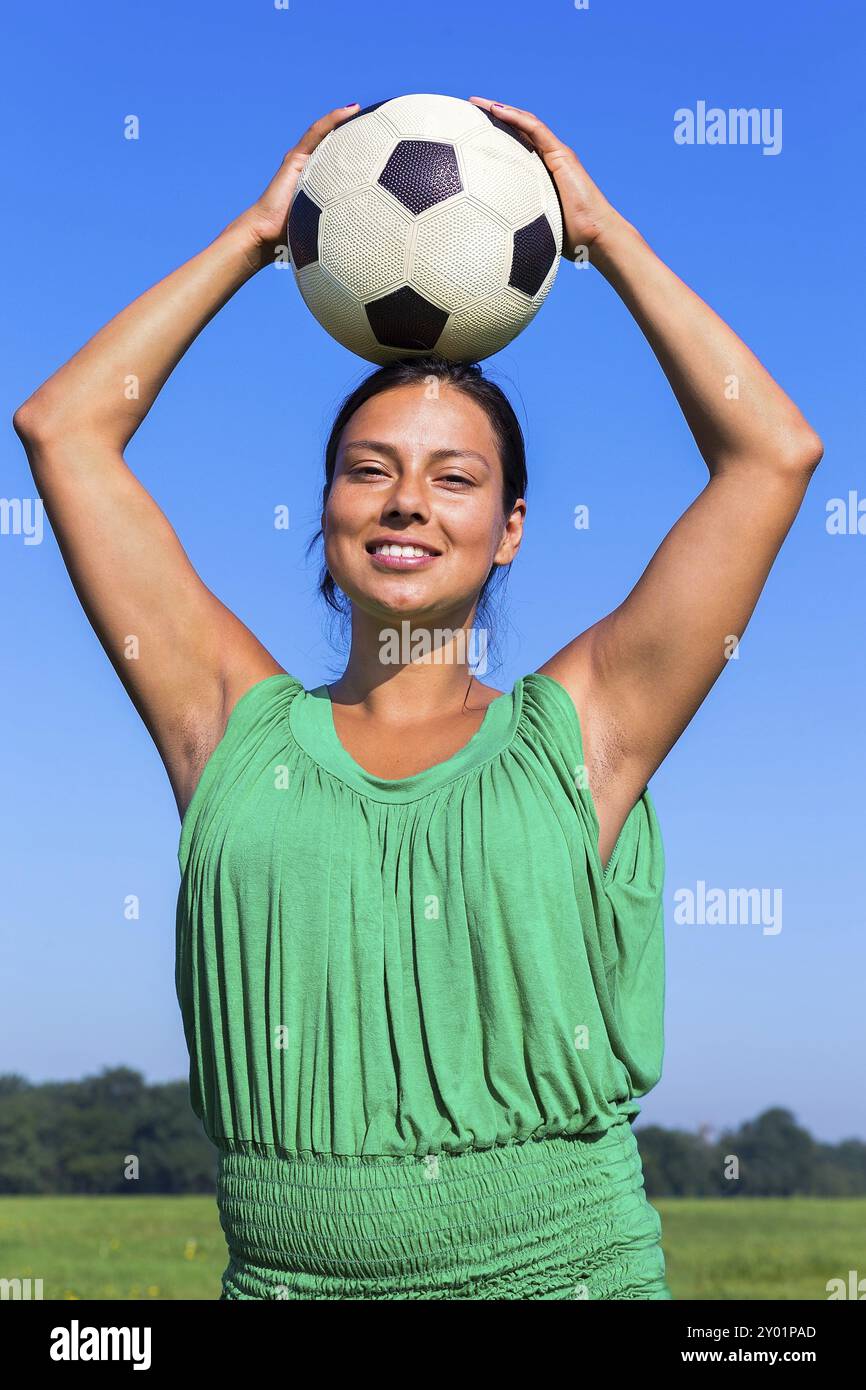 Giovane donna colombiana che tiene il calcio in testa nel cielo blu Foto Stock