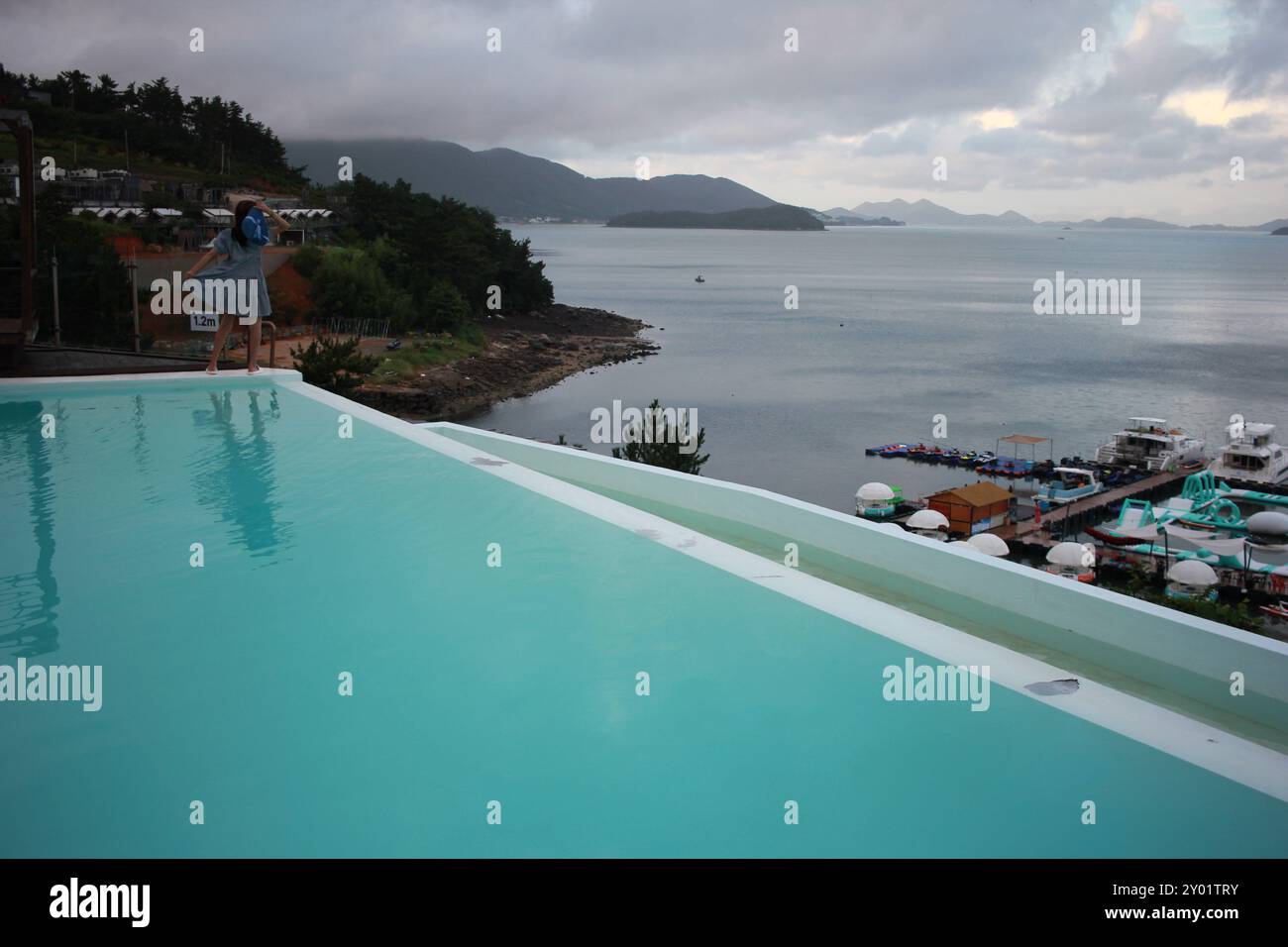 Dolsan-eup, Yeosu-si, Corea del Sud - 26 luglio 2024: Giovane donna che guarda l'alba in un resort con piscina affacciata sul mare di Yeosu Foto Stock