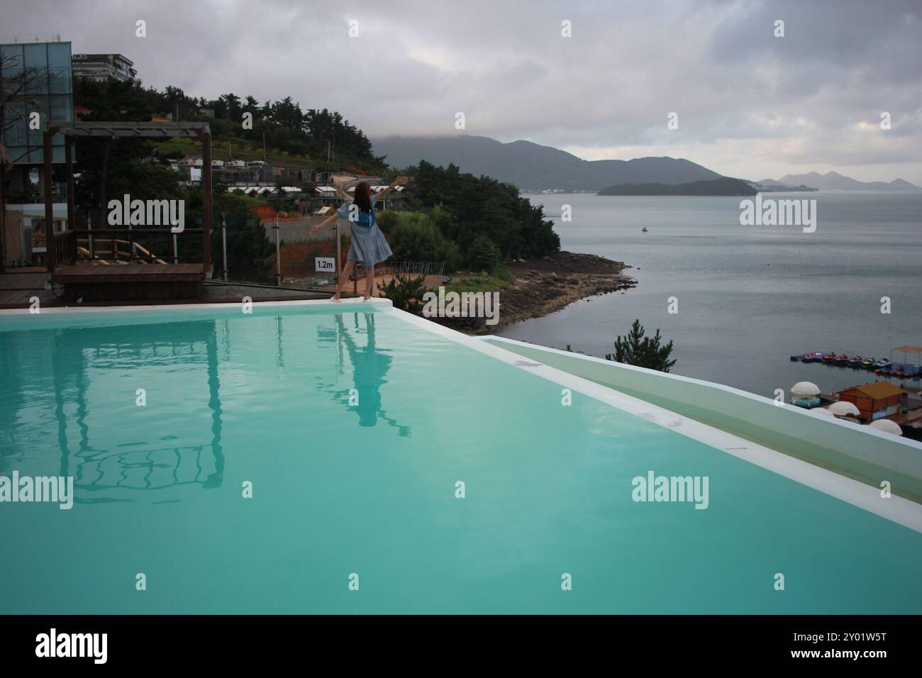 Dolsan-eup, Yeosu-si, Corea del Sud - 26 luglio 2024: Giovane donna che guarda l'alba in un resort con piscina affacciata sul mare di Yeosu Foto Stock