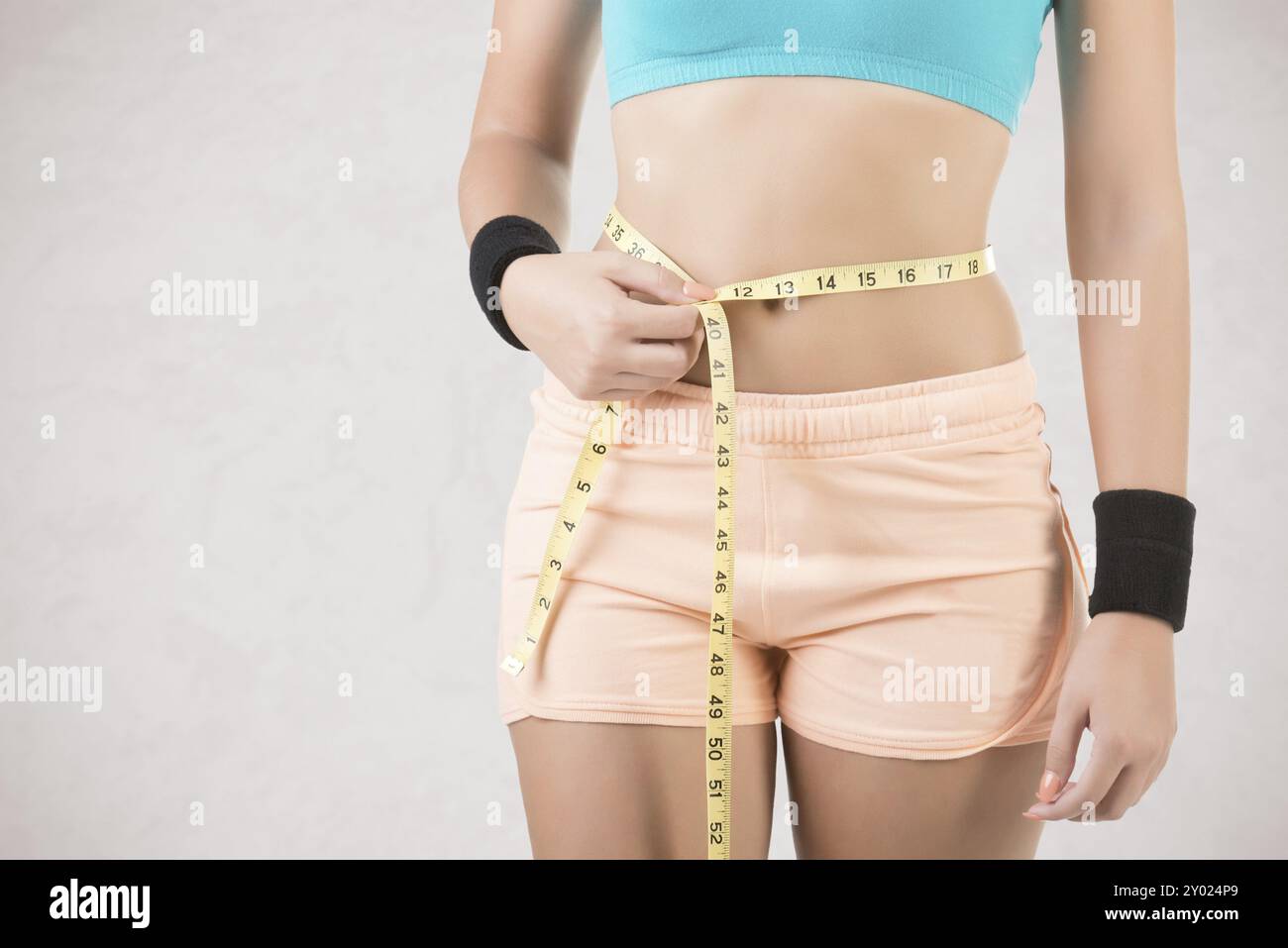 Donna misurando la sua vita con un giallo nastro di misurazione, isolato in grigio Foto Stock