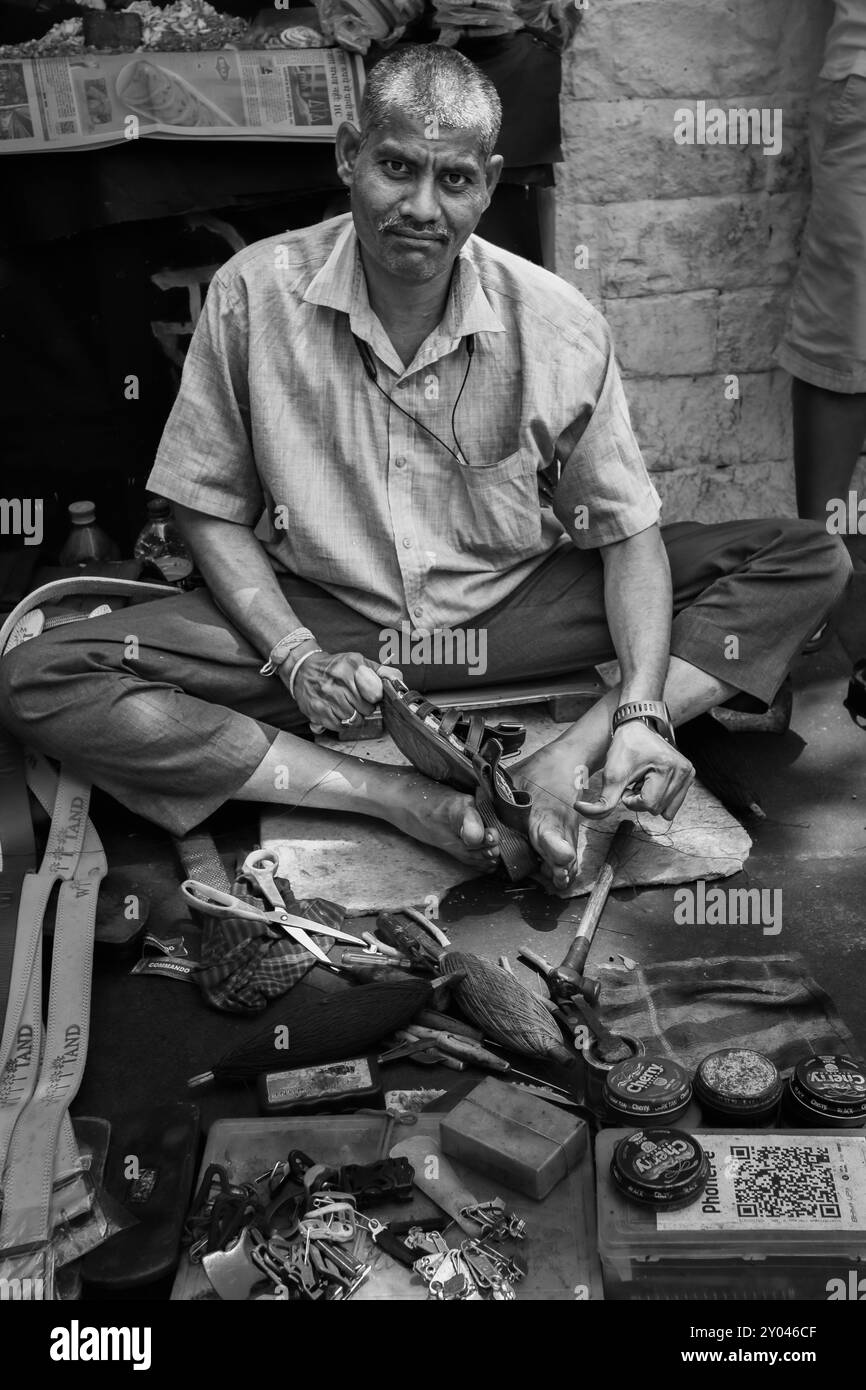 Uomo indiano locale per la riparazione di scarpe da ciottolo in una strada di Mumbai, India. Ciabattino indiano che lavora alla riparazione di scarpe nel suo negozio. Foto di viaggio, vista strada, editor Foto Stock