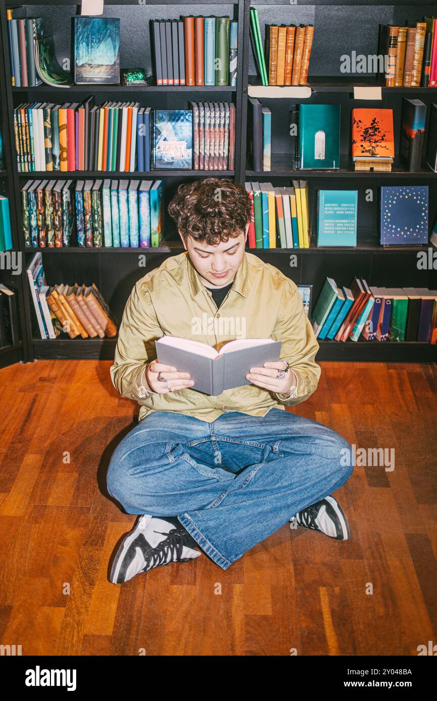Giovane che legge un libro seduto sul pavimento in libreria Foto Stock
