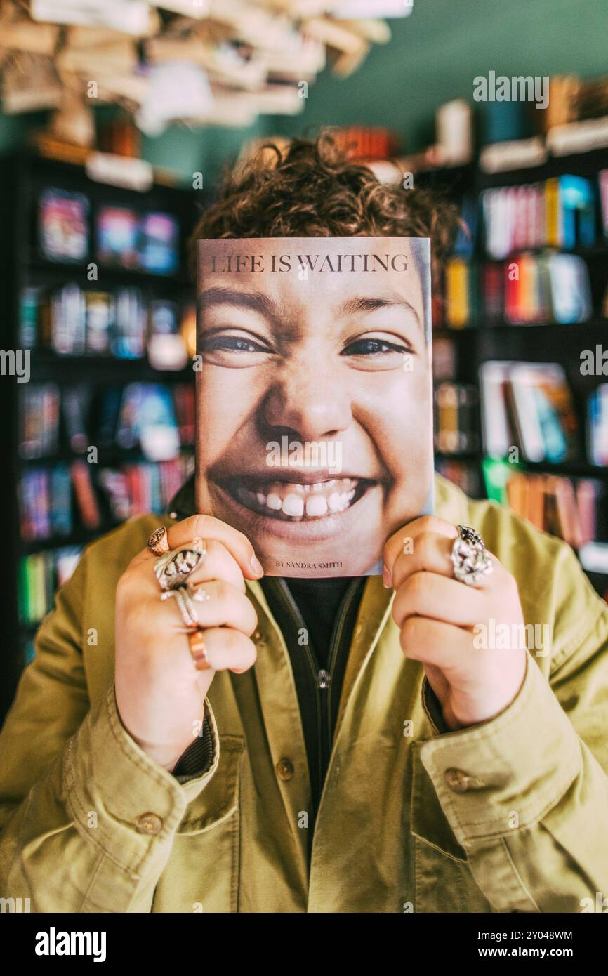 Giovane che tiene un libro davanti al viso in libreria Foto Stock