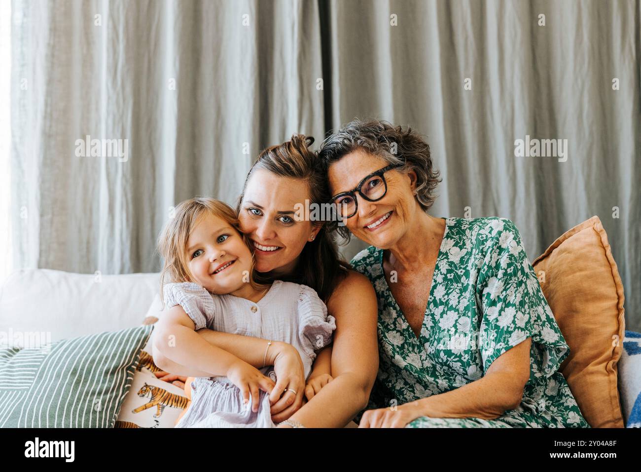Ritratto di madre sorridente seduta con figlia e donna anziana sul divano di casa Foto Stock