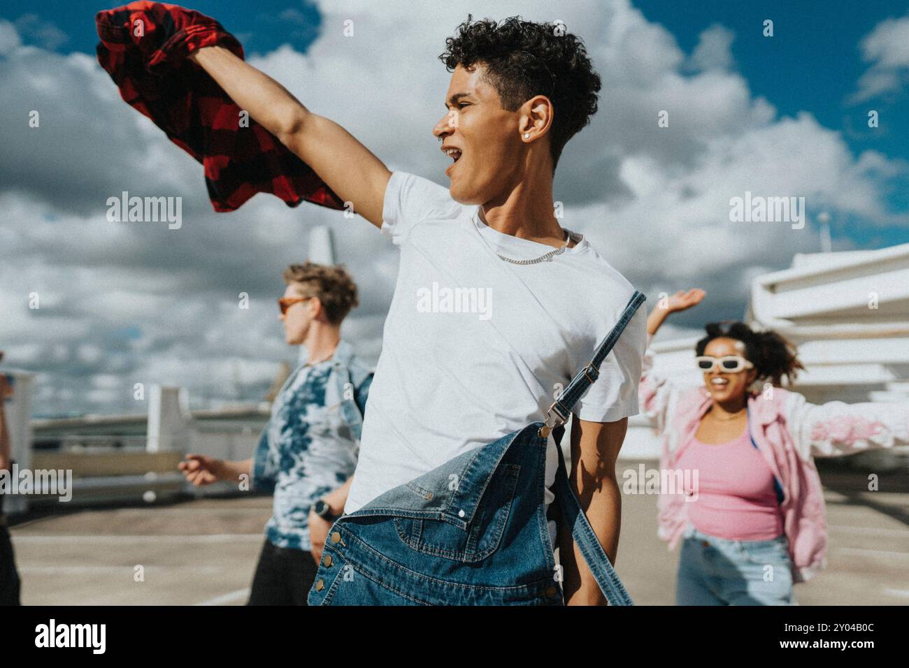 Allegro hipster in tuta bavaglino che ballano con amici maschi e femmine nel parcheggio Foto Stock