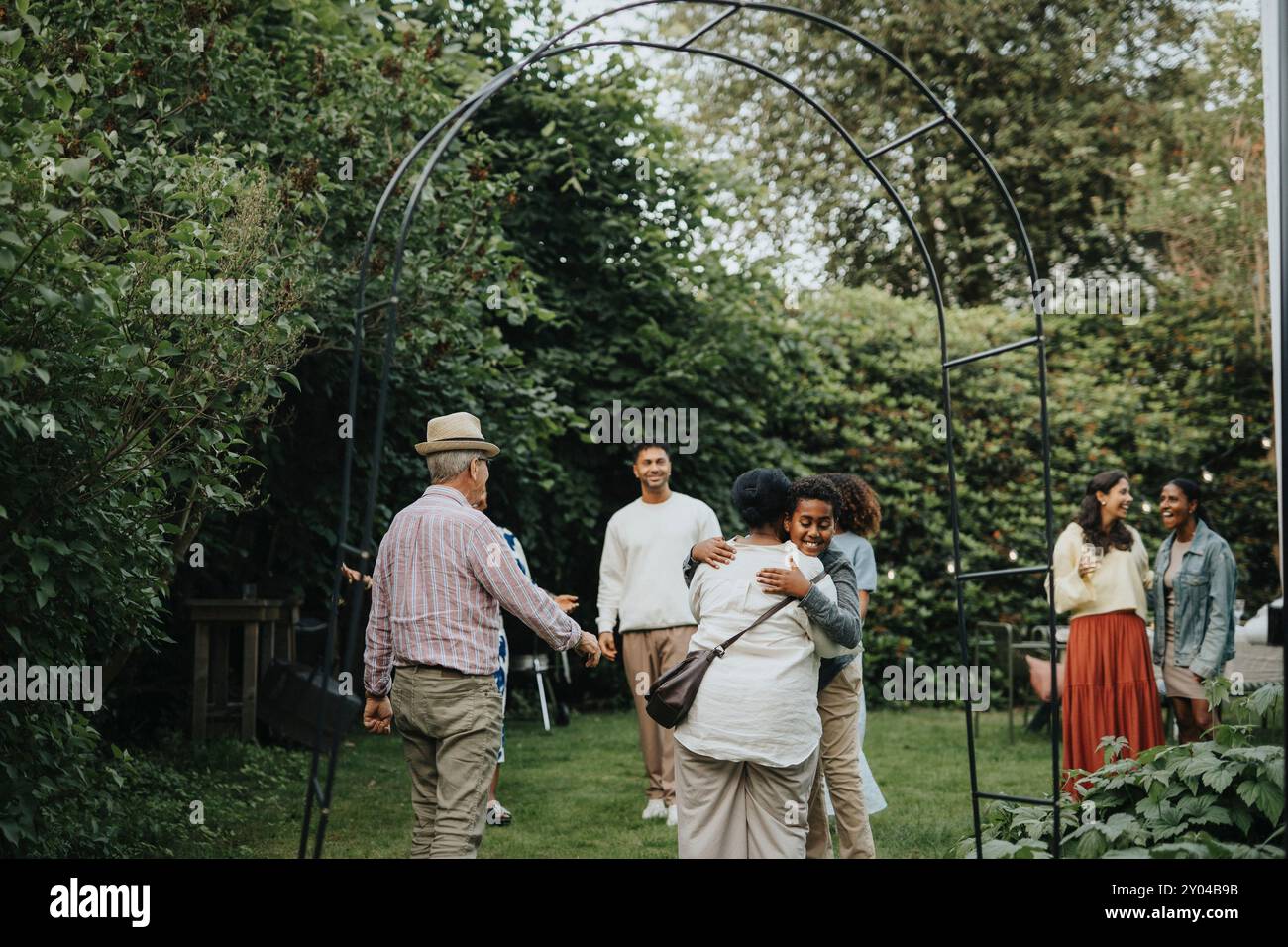 I membri della famiglia, uomini e donne felici, accolgono i nonni durante la riunione sociale alla festa in giardino Foto Stock