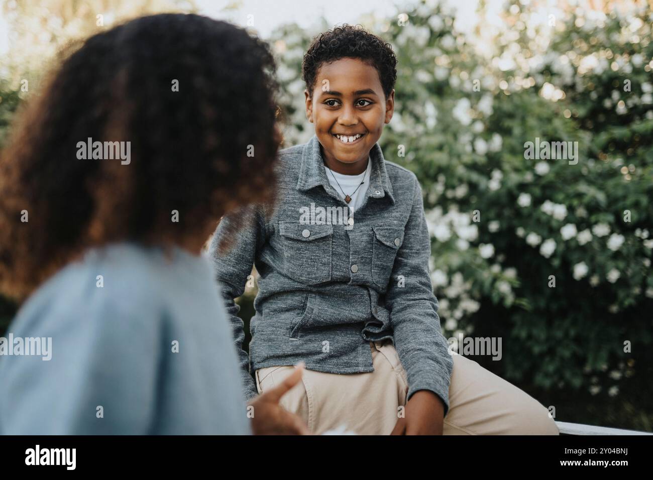 Un ragazzo sorridente che parla con la sorella nel cortile posteriore Foto Stock