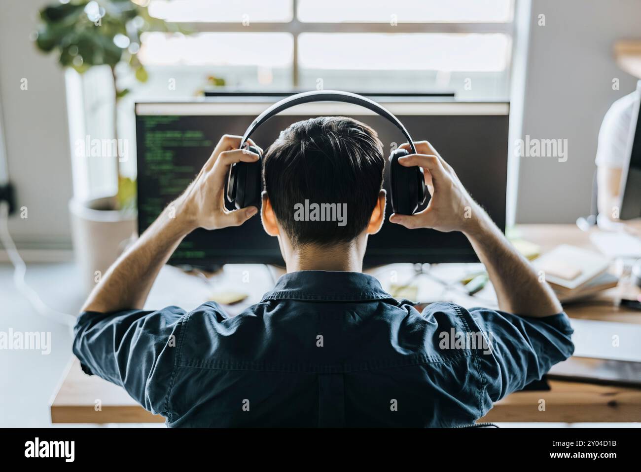 Vista posteriore del programmatore maschio che indossa le cuffie in ufficio Foto Stock