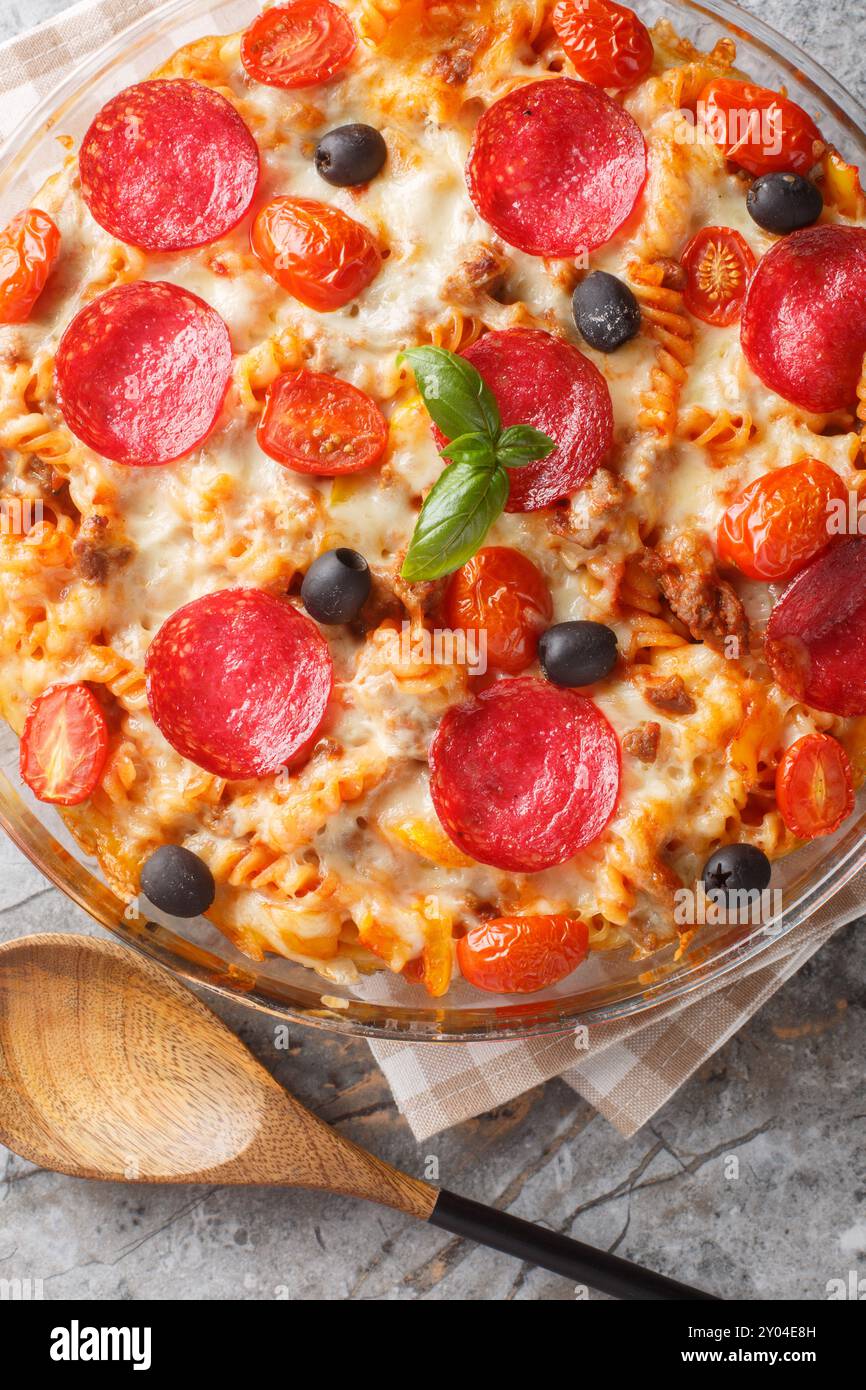 Sostanziosa casseruola per pasta fusilli con formaggio, pomodori, carne macinata fritta, salsiccia di salame, peperoni e olive con salsa marinara primo piano in un bicchiere di Foto Stock